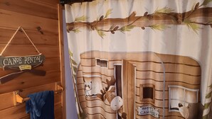 Un bagno con tenda da doccia in legno a tema baita, un portasciuga e un cartello con i prezzi del noleggio canoe.
