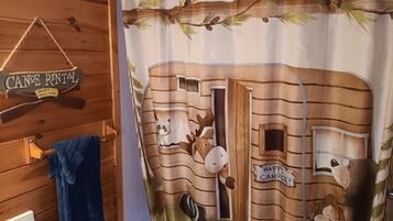Un baño con cortina de ducha de estilo rústico de cabaña, un perchero y un letrero que indica las tarifas de alquiler de canoas.