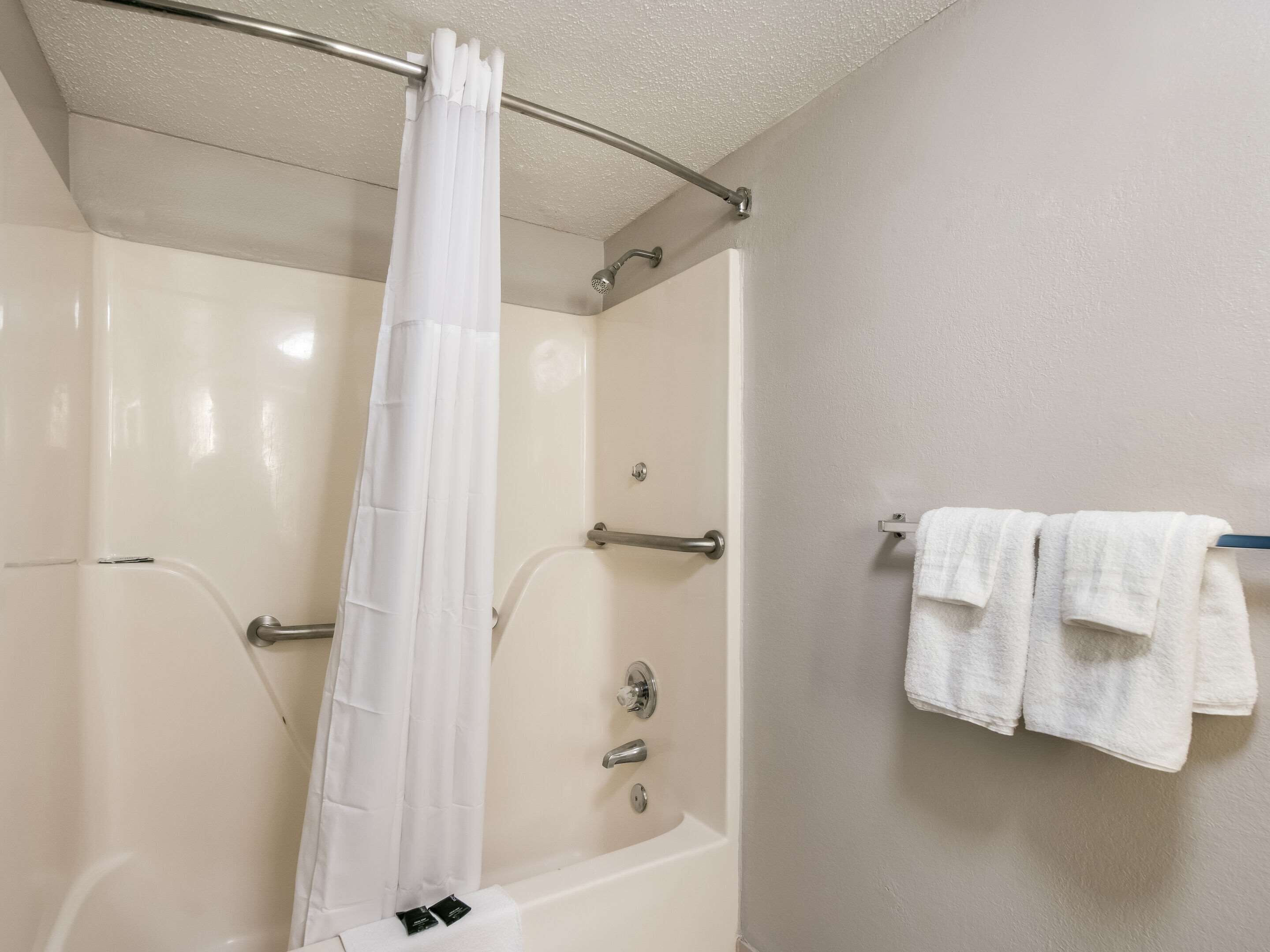 A bathroom with a bathtub, a shower curtain, and a towel rack with towels.