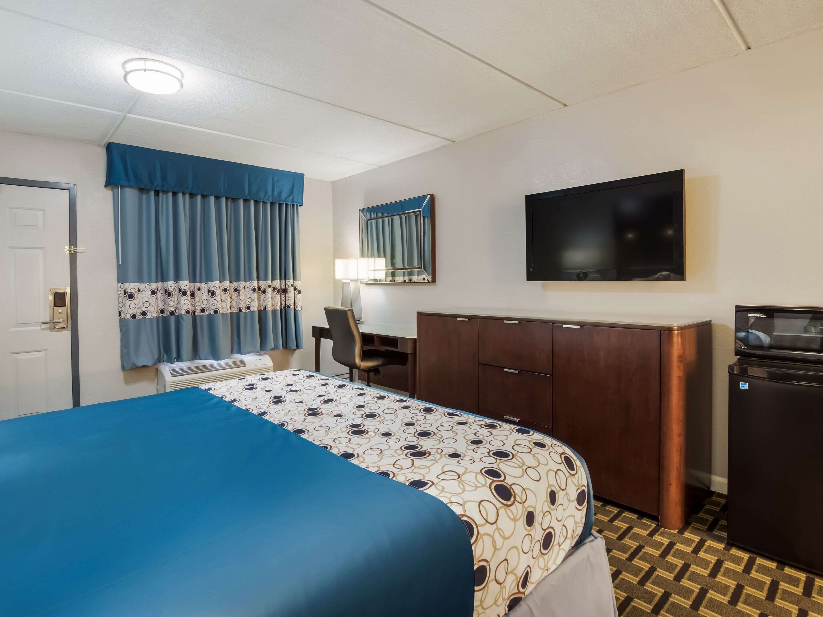 A hotel room with a bed, a desk, a chair, a television, a wardrobe, and a microwave.