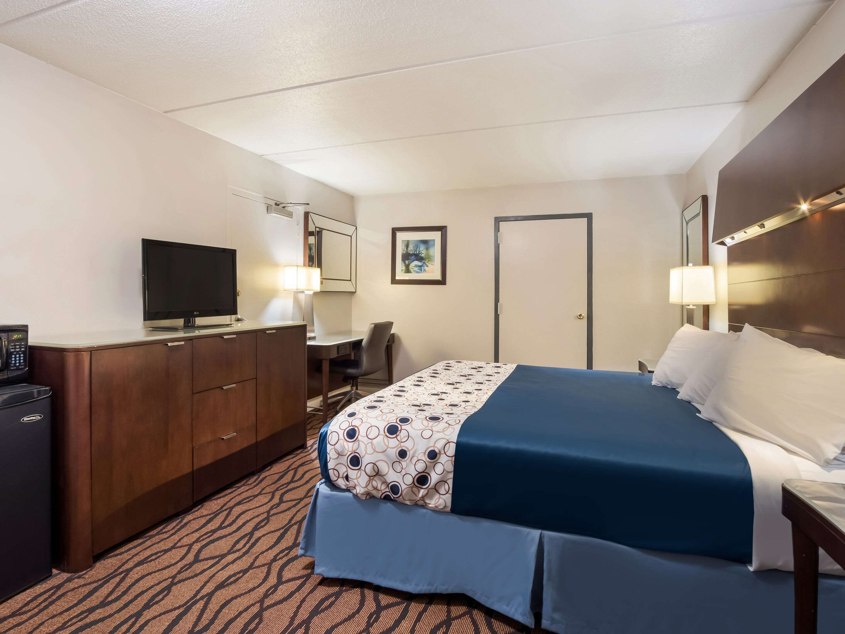 Una habitación de hotel con una cama, un escritorio, un televisor y un mini bar.