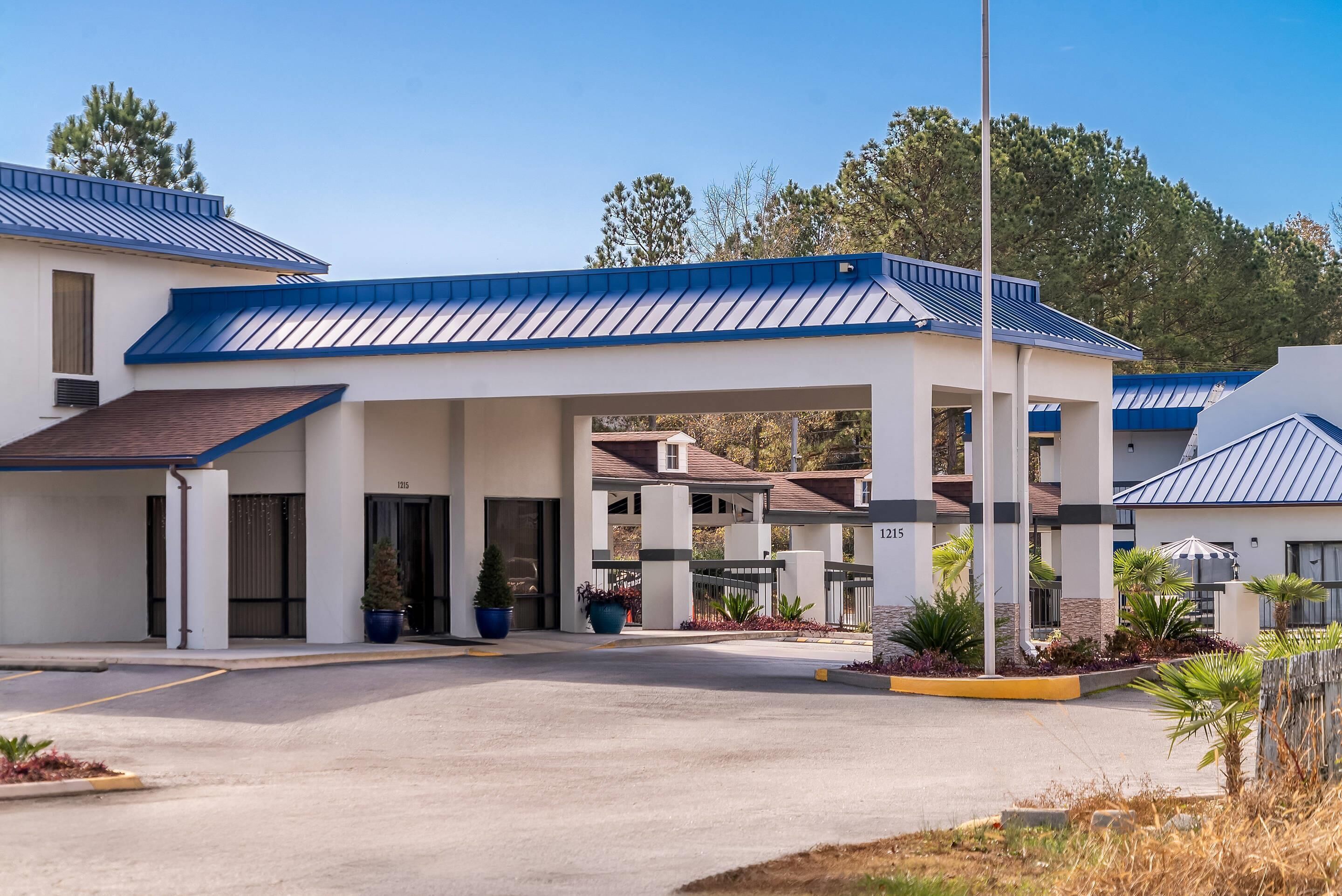 Un hotel moderno con estacionamiento techado, varias entradas y un acceso arbolado.