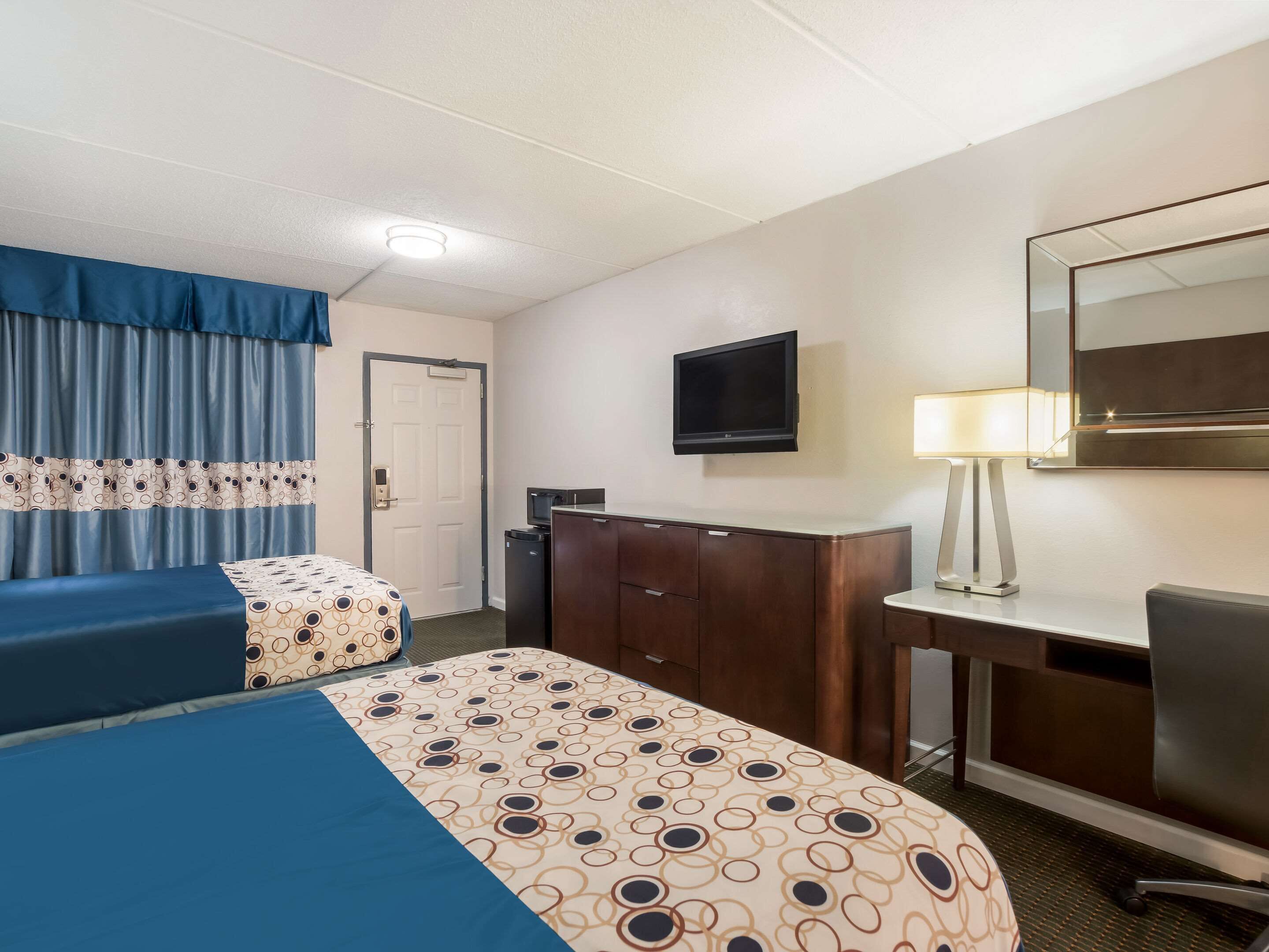 Quarto de hotel com duas camas, uma escrivaninha, uma cadeira, uma televisão e um abajur.