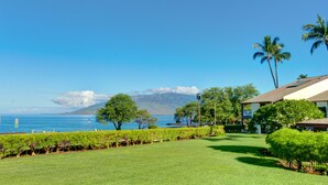A lush green lawn, palm trees, and a view of the ocean with mountains in the background. -  #239 Steps to Kamaole III Beach,  New Kitchen 'Solid Gold Value' Maui Revealed (Kihei)