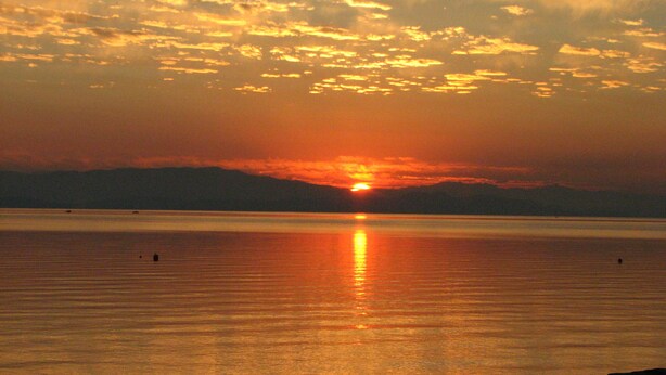 A sunset over a calm body of water with a distant landmass. - Seaside Beach Croft Cabin (Qualicum Beach)