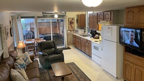 A compact living space with a sofa, a chair, a small table, a kitchen area with wooden cabinets, a refrigerator, a microwave, and a television. - Seaside Beach Croft Cabin (Qualicum Beach)