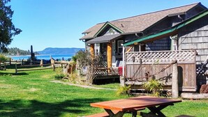 A rustic wooden cabin with a picnic table in the foreground, surrounded by a well-maintained lawn and a wooden fence. - Seaside Beach Croft Cabin (Qualicum Beach)