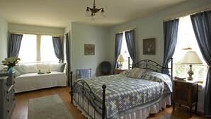 A bedroom with a large bed, a bedside table with a lamp, a dresser, and a chair. - Historic 6-bedroom manor next to Beaverkill River — sleeps 18, 5 en-suite baths. (East Branch)