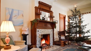 A cozy living room with a fireplace, a Christmas tree, and a patterned rug. - Historic 6-bedroom manor next to Beaverkill River — sleeps 18, 5 en-suite baths. (East Branch)