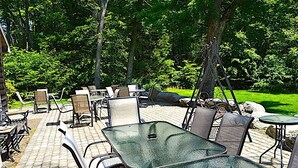 An outdoor patio with metal tables and chairs, surrounded by trees and a grassy area.