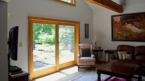 A living room with a large sliding glass door, a television, a plaid armchair, a wooden coffee table, and a painting on the wall.