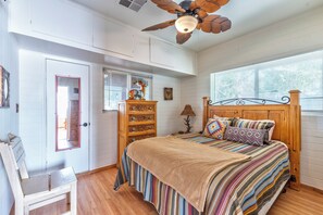 Un dormitorio con cama, cómoda, espejo, ventilador de techo y ventana con persianas.