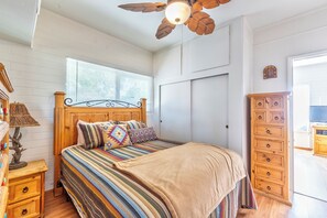 A bedroom with a wooden bed, striped bedding, a ceiling fan, a wooden dresser, and a window with blinds.