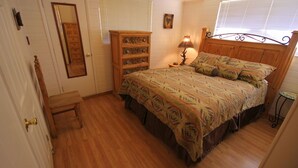 Een slaapkamer met een houten bed, een nachtkastje met lamp, een dressoir en een spiegel aan de muur.