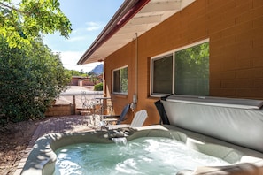 Een hottub in een achtertuin met een bakstenen muur, een raam en een patio tafel.