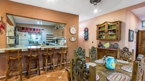 Zona pranzo con un grande tavolo in legno, diverse sedie e una cucina sullo sfondo.