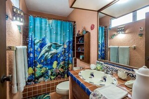 Un baño con cortina de ducha con motivos marinos, un inodoro, un lavabo con recipiente decorativo y un espejo.