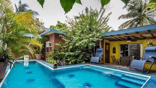 Una piscina con acqua cristallina circondata da vegetazione rigogliosa e un edificio con tetto blu.