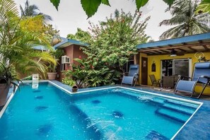 A swimming pool with clear blue water, surrounded by lush greenery and a building with a blue roof. - Tropical and Conveniently Located Close to Everything (Cozumel)