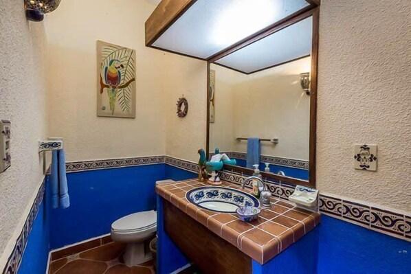 A bathroom with a blue and white tiled wall, a wooden vanity, a white toilet, and a large mirror. - Tropical and Conveniently Located Close to Everything (Cozumel)