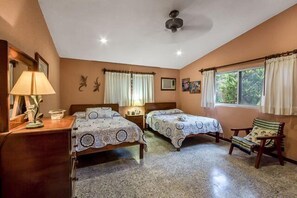 Un dormitorio con dos camas, un escritorio con lámpara, una silla y un ventilador de techo.