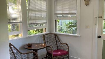 A corner room with a bay window, wicker chairs, a small table, and a patterned rug.