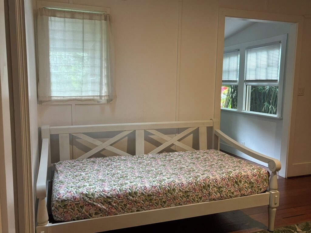 Una cama individual con colcha estampada en una habitación con paredes blancas y una ventana con persianas.