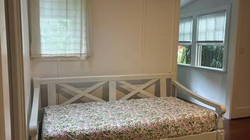 Una cama individual con colcha estampada en una habitación con paredes blancas y una ventana con persianas.