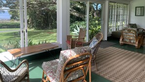 A sunlit room with large windows, wicker furniture, and a view of a lush garden. - Historic Upcountry Maui Property With Pool, 7Bedrooms, Sleeps 16 (Makawao)