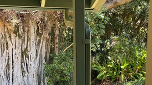 A covered outdoor seating area with a chair, a tree, and a grassy garden. - Historic Upcountry Maui Property With Pool, 7Bedrooms, Sleeps 16 (Makawao)