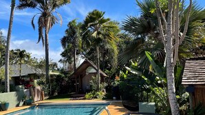 A swimming pool with a wooden deck, surrounded by palm trees and tropical plants. - Historic Upcountry Maui Property With Pool, 7Bedrooms, Sleeps 16 (Makawao)