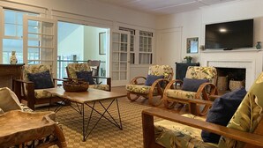A spacious living room with wicker furniture, a fireplace, and a large TV mounted above it. - Historic Upcountry Maui Property With Pool, 7Bedrooms, Sleeps 16 (Makawao)