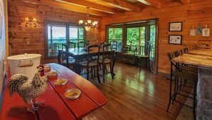 A wooden cabin interior with a dining area, wooden walls, and large windows.