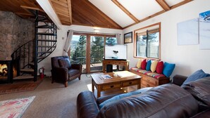 A cozy living room with a fireplace, a wooden staircase, and a large window with a view of the outdoors.