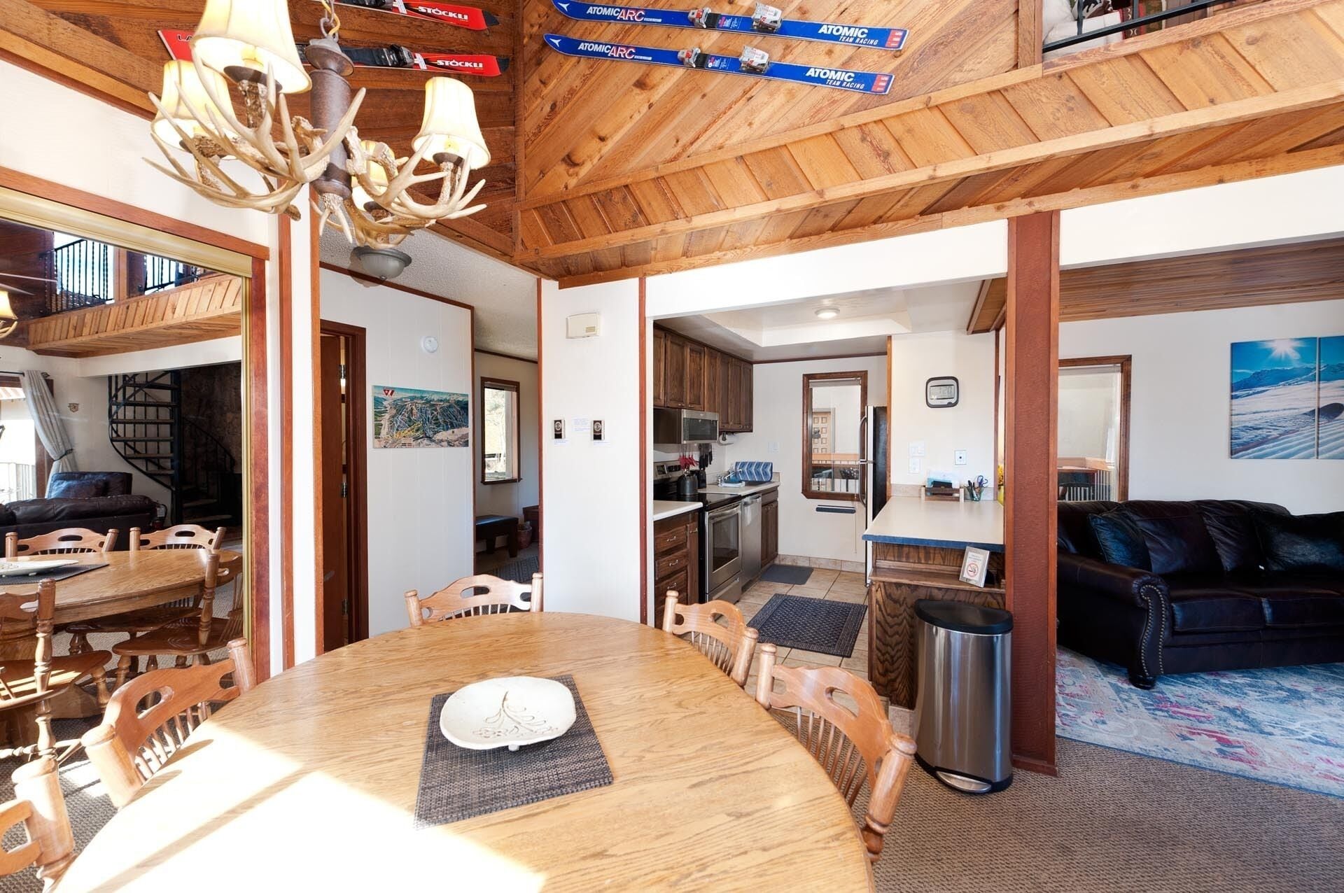 A wooden interior with a dining table, chairs, a chandelier, and a kitchen area.