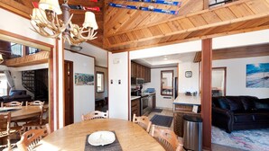 A spacious living area with a wooden ceiling, a dining table with chairs, a sofa, and a kitchen in the background.