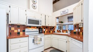 Una cocina con armarios blancos, microondas, estufa y lavavajillas. En la pared, un cartel dice 'Queen of the Kitchen'.
