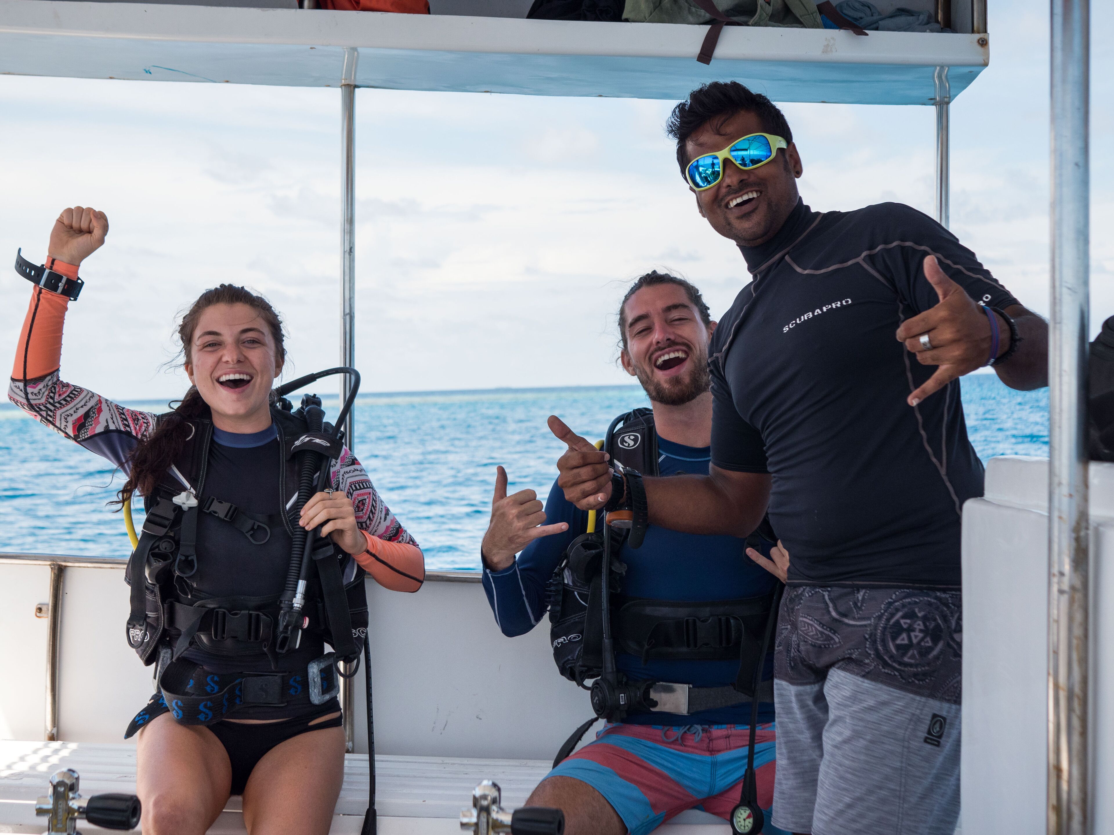 Three people on a boat wearing scuba diving gear.