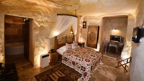 A bedroom with a bed, bedside table, lamp, and a television mounted on the wall. - Nostalji Cave Suit Hotel (Ürgüp)