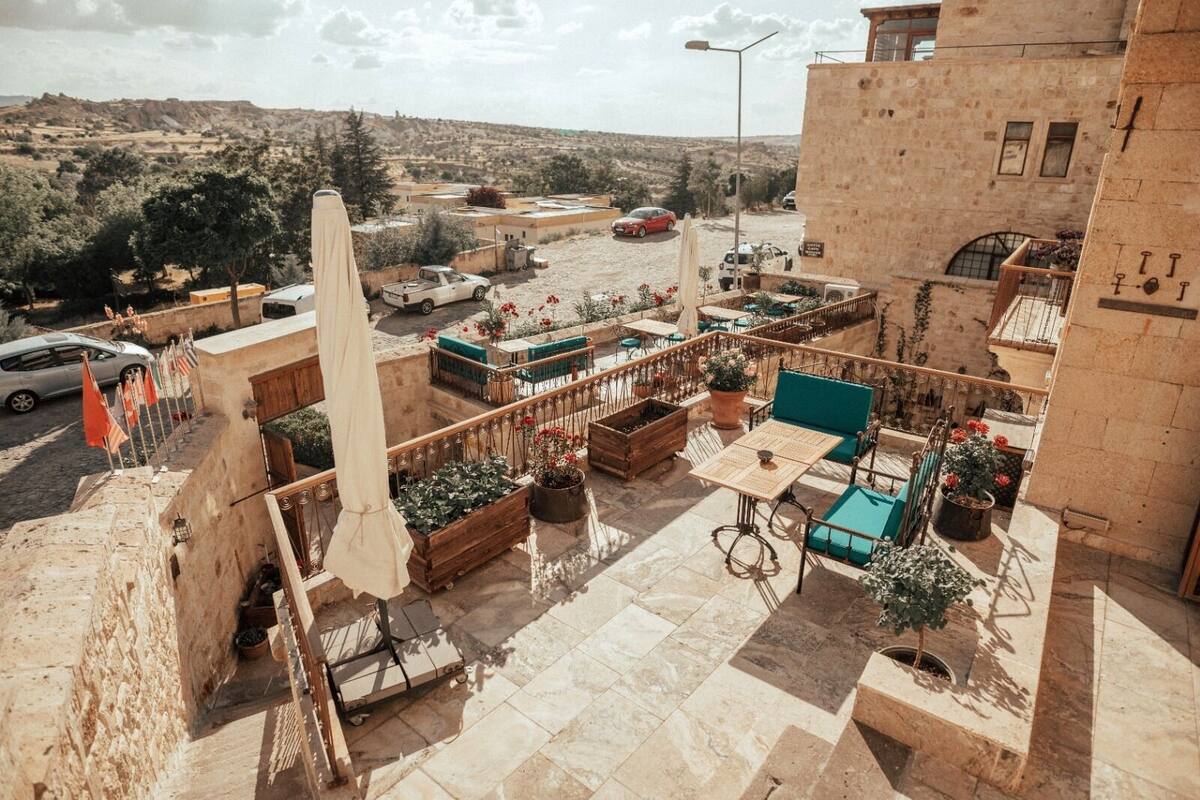 Un patio al aire libre con mesas y sillas, rodeado de muros de piedra y plantas en macetas.