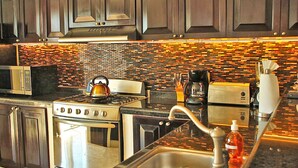 A modern kitchen with dark wood cabinets, a tiled backsplash, stainless steel appliances, and a granite countertop. - Villa Izcalli by PRP (Playa del Carmen)