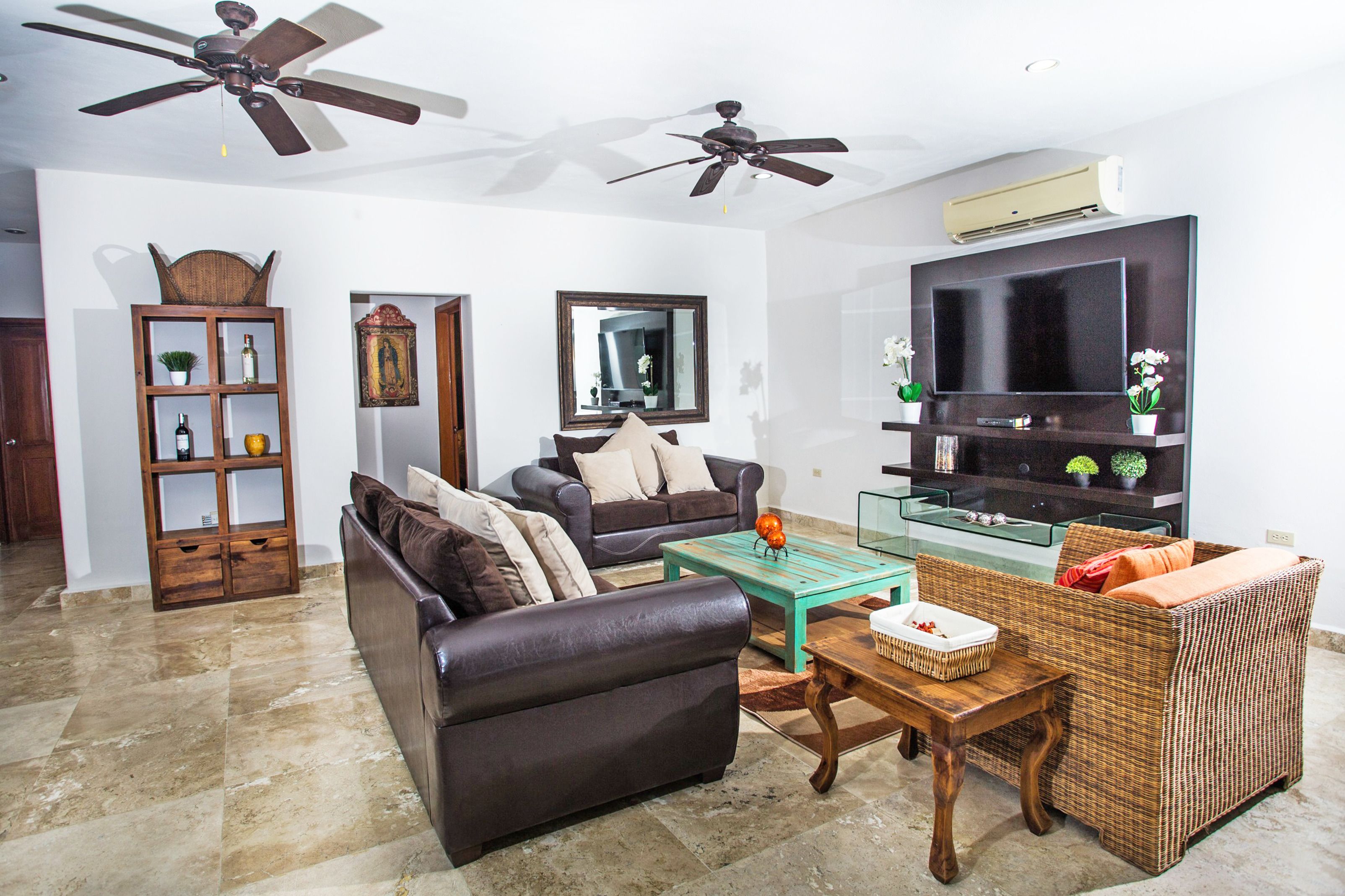 A living room with a dark brown sofa, a wicker chair, a glass coffee table, and a flat-screen TV on a wooden stand.