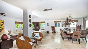 A spacious living area with a sofa, wicker chairs, a glass coffee table, and a dining area with a long table and chairs. - Villa Izcalli by PRP (Playa del Carmen)