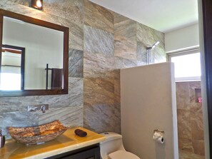 Ein Badezimmer mit Steinwand, Spiegel mit Holzrahmen, einem Aufsatzwaschbecken, Toilette und Dusche.