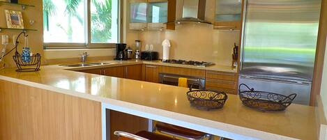 A modern kitchen with a large island, stainless steel appliances, and a view of the outdoors.