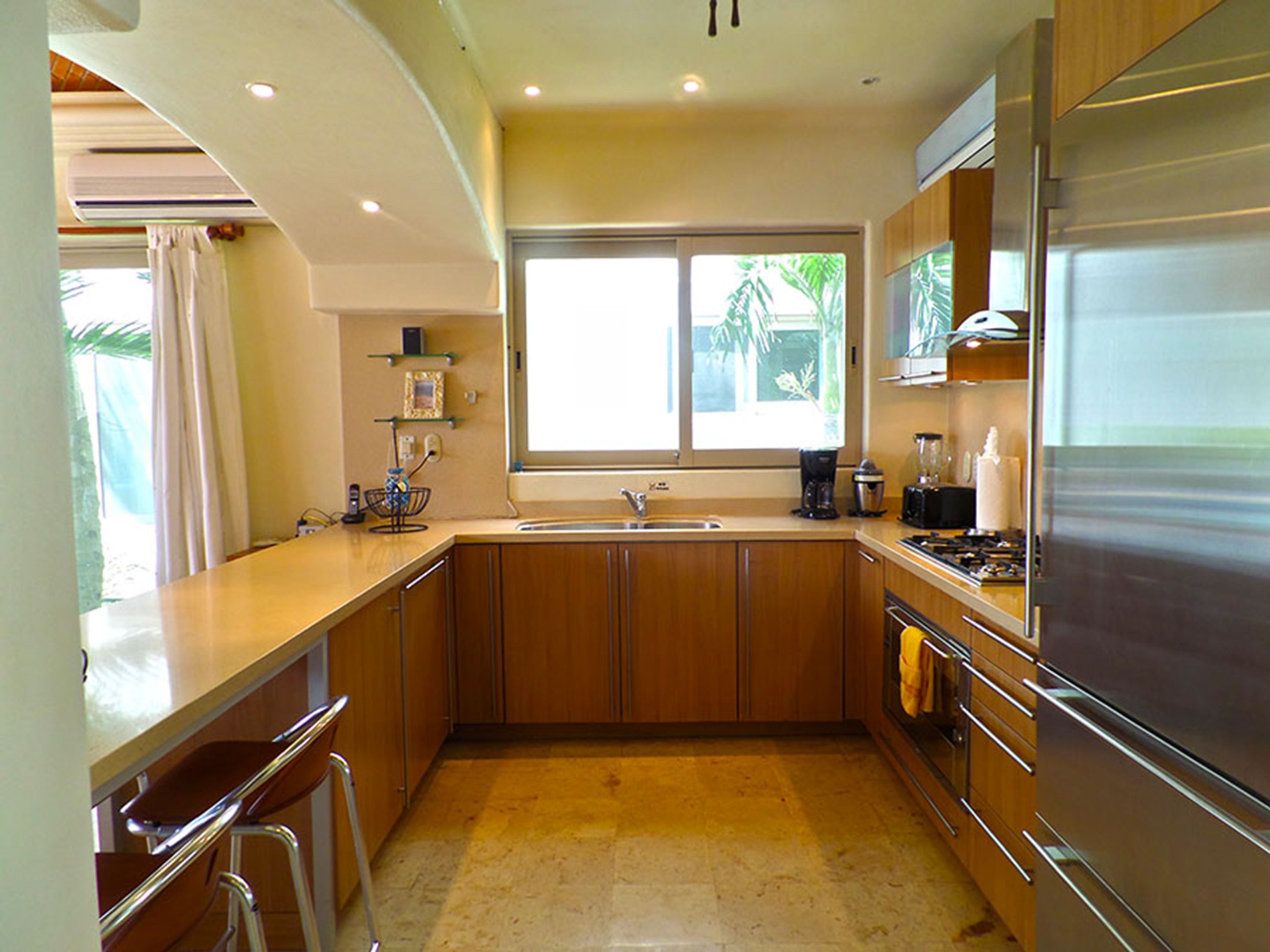 Una cocina moderna con armarios de madera, un refrigerador de acero inoxidable y un ventanal que proporciona luz natural.