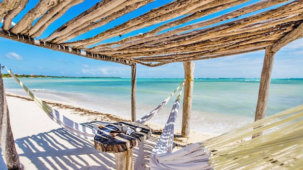 Una hamaca bajo una estructura de madera en una playa con agua turquesa cristalina.