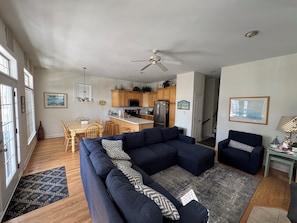 A living room with a sectional sofa, a dining area with a table and chairs, a kitchen with wooden cabinets and appliances, and a ceiling fan.
