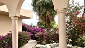 A covered outdoor area with a stone pathway, surrounded by large rocks and flowering plants.