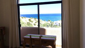 A room with a view of the sea, a wooden table, and a window with curtains.